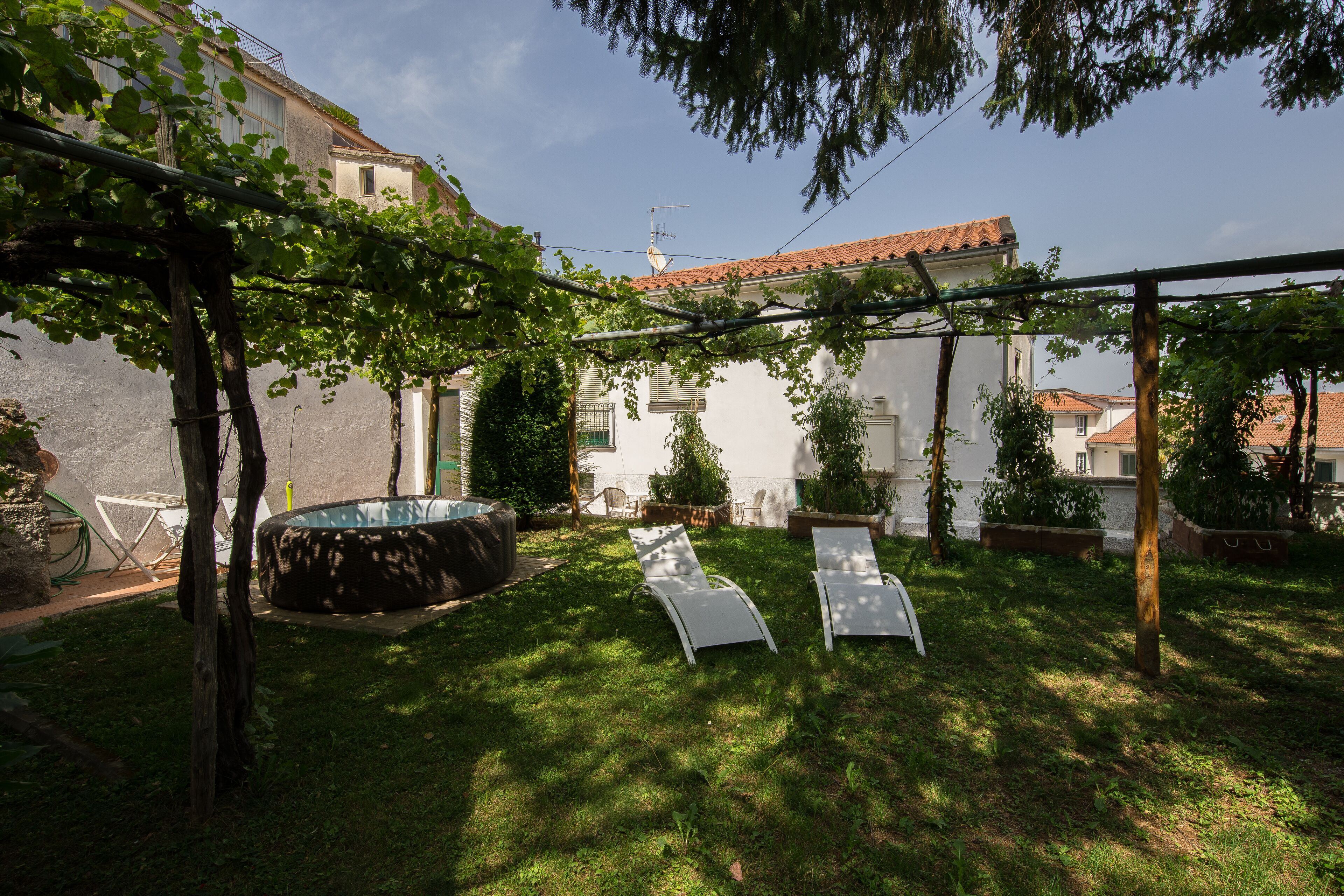 A backyard with a hot tub, two lounge chairs, and a pergola with climbing plants.
