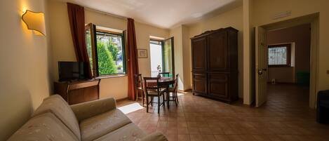A living room with a sofa, a TV, a dining table with chairs, a cabinet, and a window with curtains.