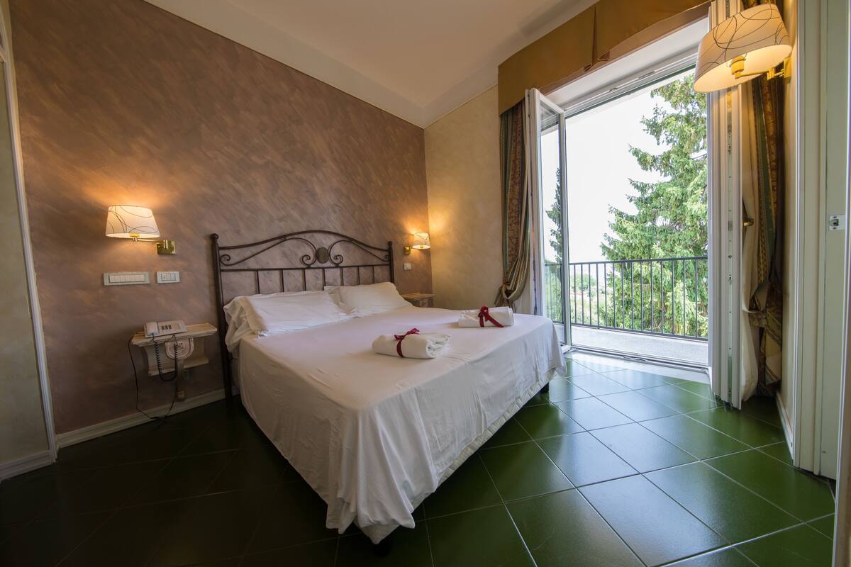 A hotel room with a large bed, two bedside lamps, a telephone, and a view of the outdoors through a balcony.