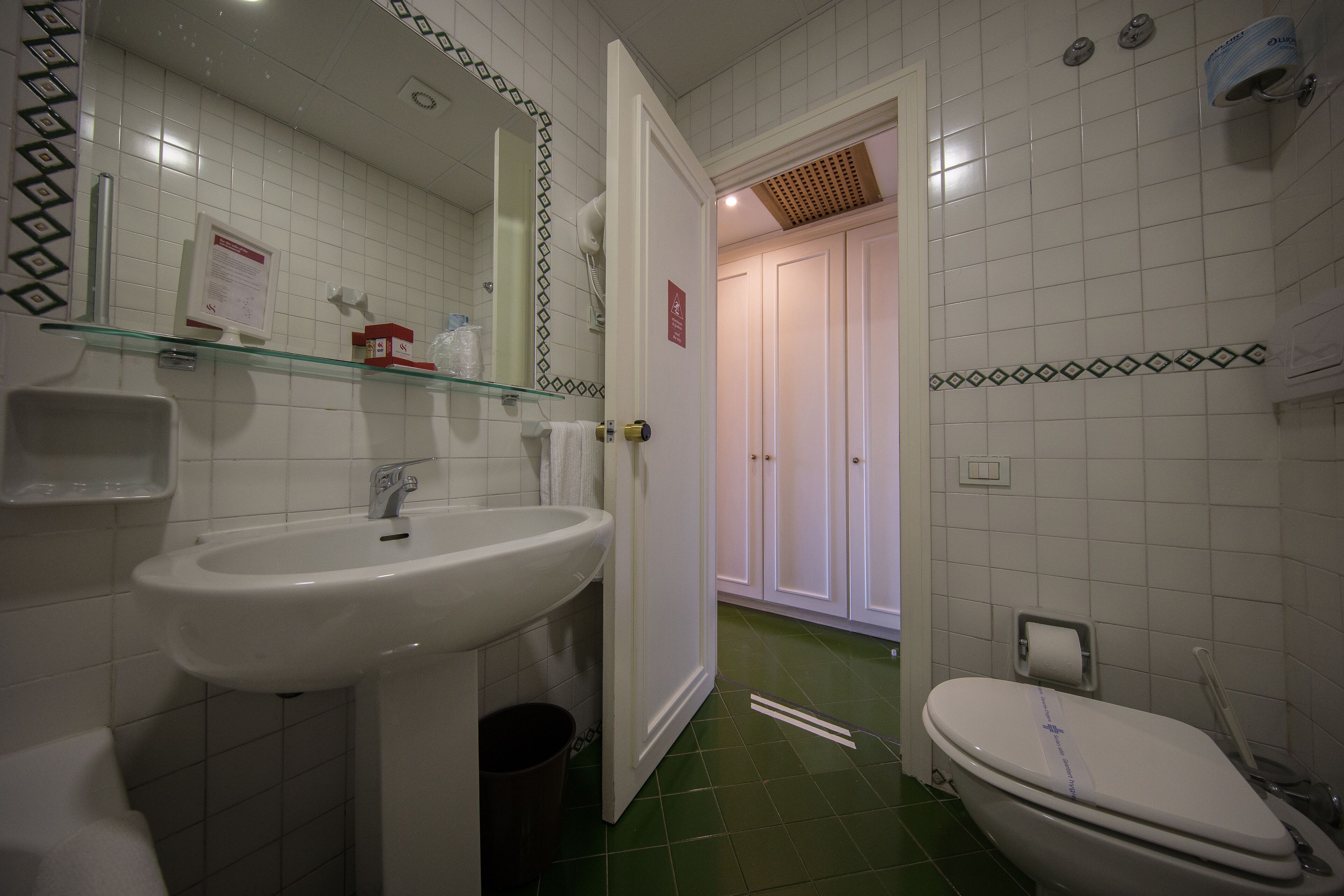 Une salle de bain avec un lavabo blanc, une étagère en verre, des toilettes et un miroir.
