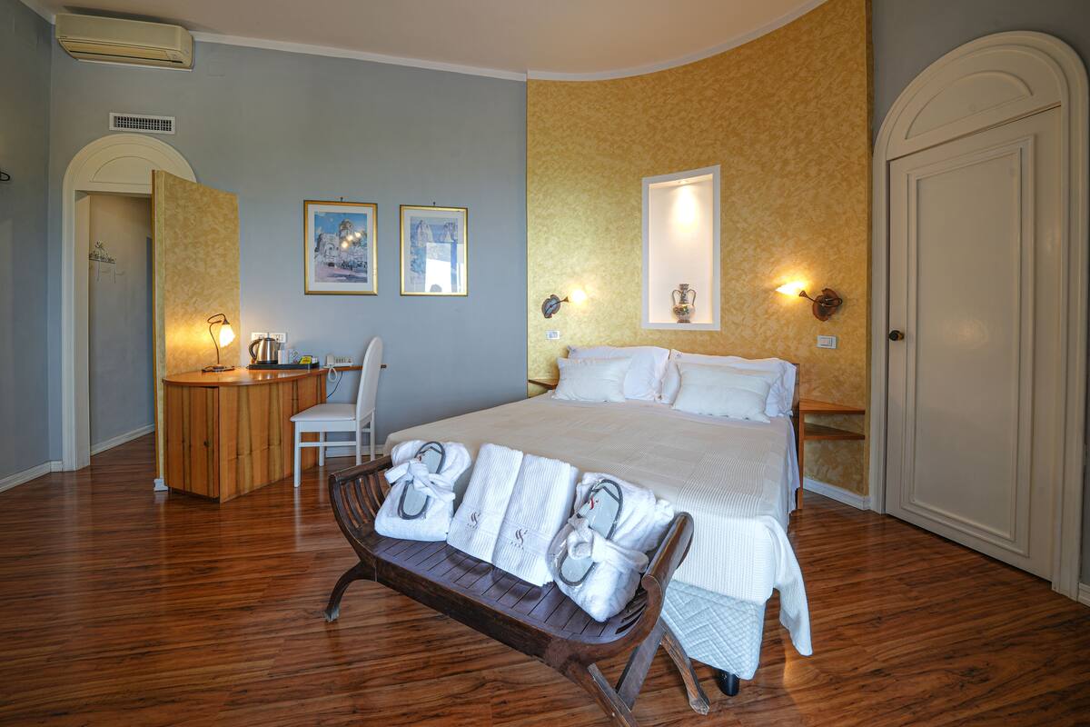 A bedroom with a bed, a desk, a chair, and a bench with towels.
