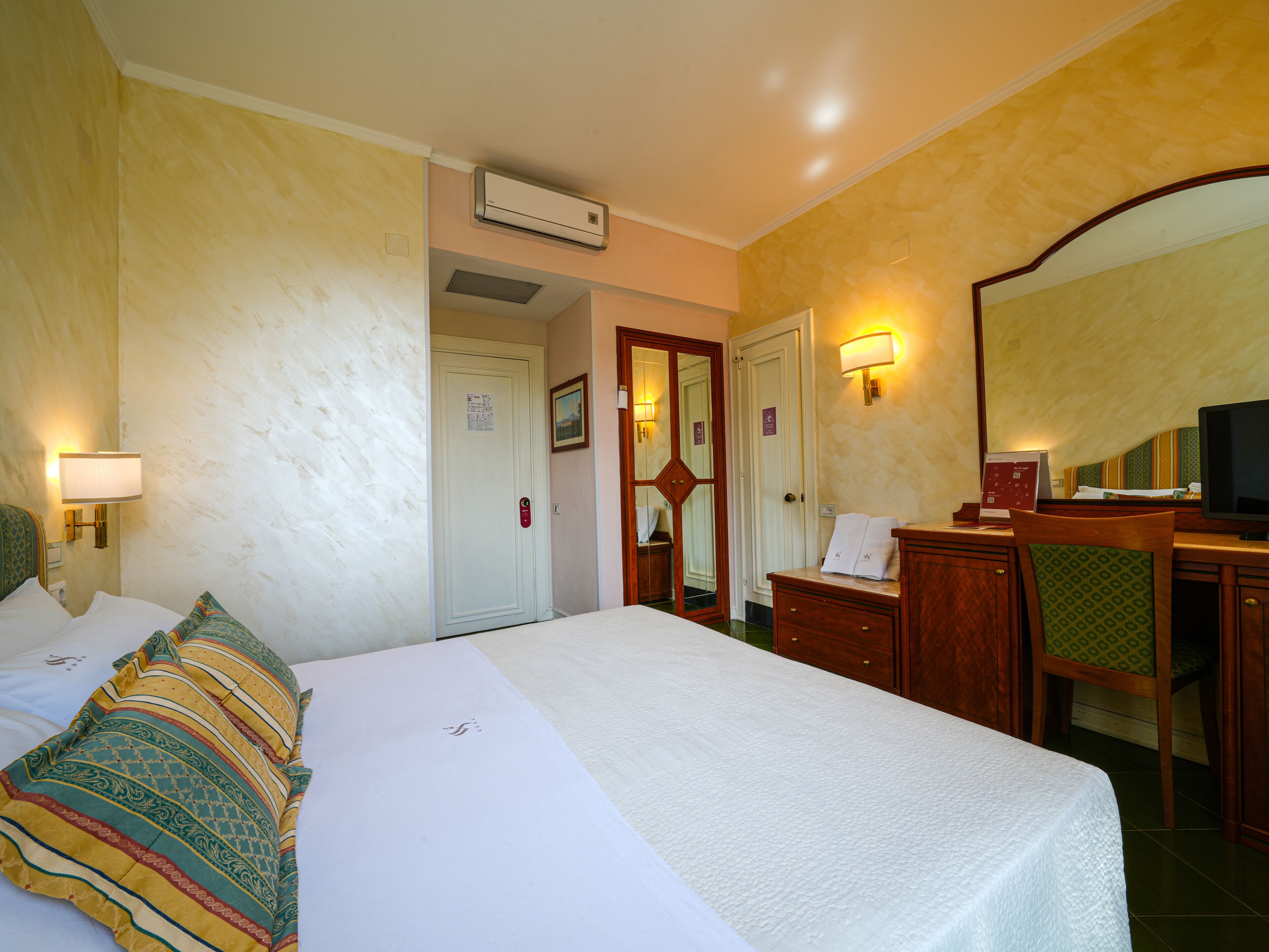 Hotelkamer met een bed, bureau, stoel, spiegel en een wandairconditioner.