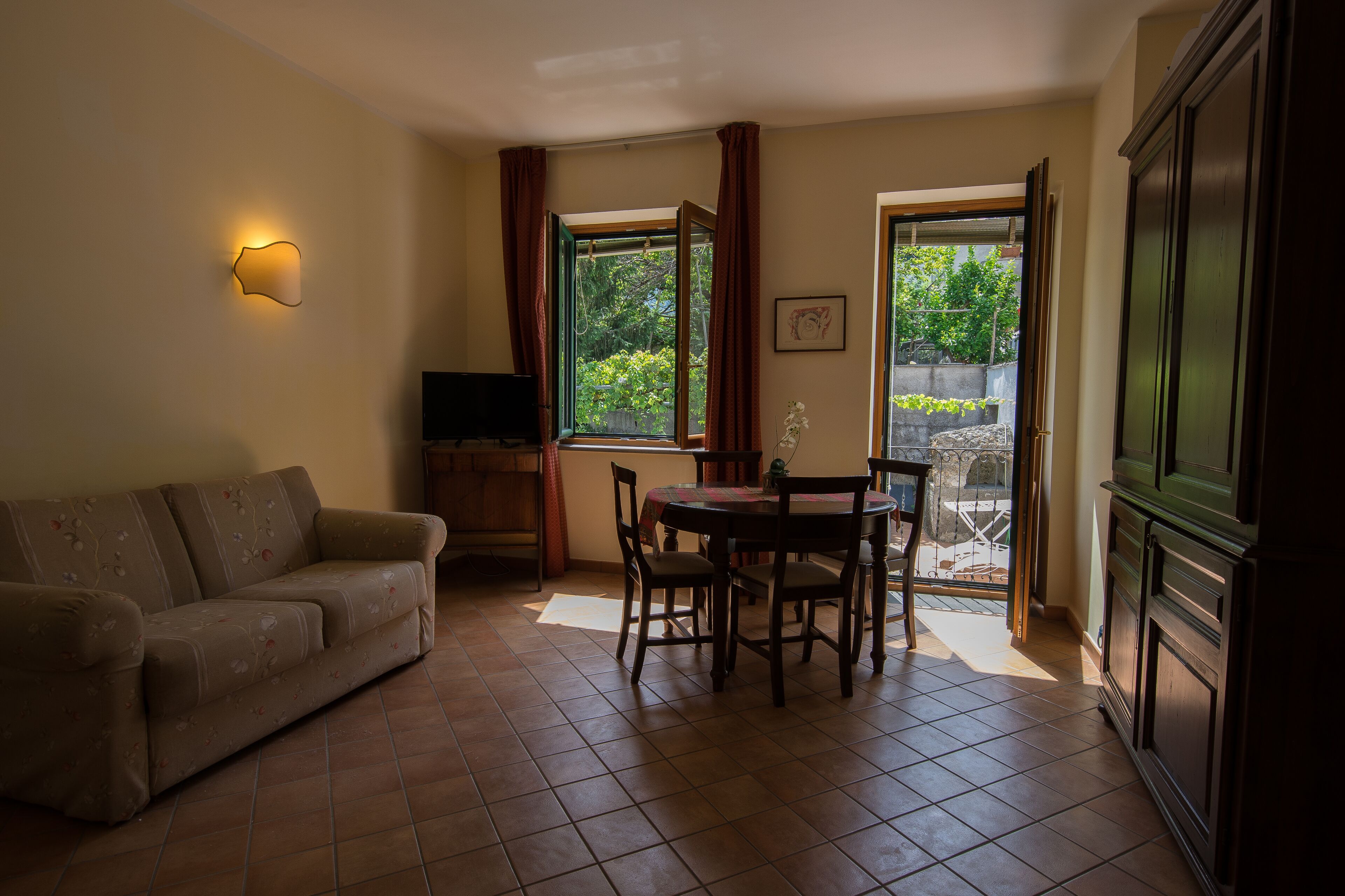 A living room with a sofa, a dining table with chairs, a TV, and a window with curtains.