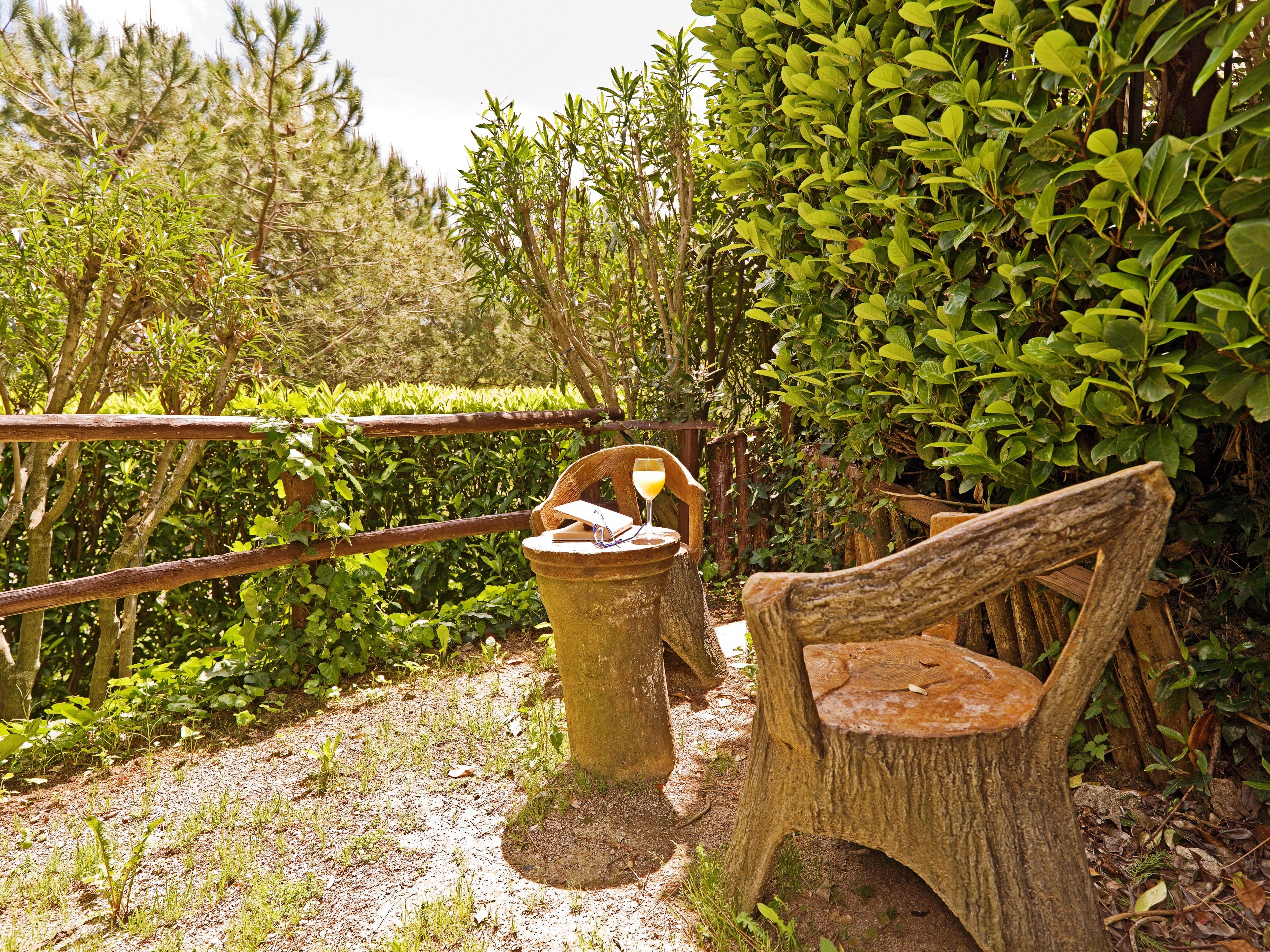 A rustic outdoor seating area with a wooden chair and a concrete planter with a book and a glass.