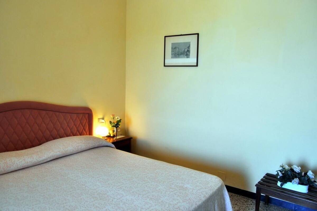 Una habitación de hotel con una cama, una mesita de noche, un cuadro en la pared y una pequeña mesa con flores.
