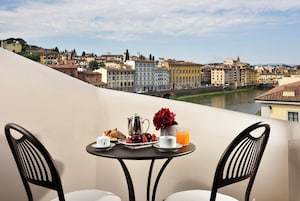 Un balcón con una mesa lista para el desayuno, con vistas a un paisaje urbano que incluye edificios históricos y un río.