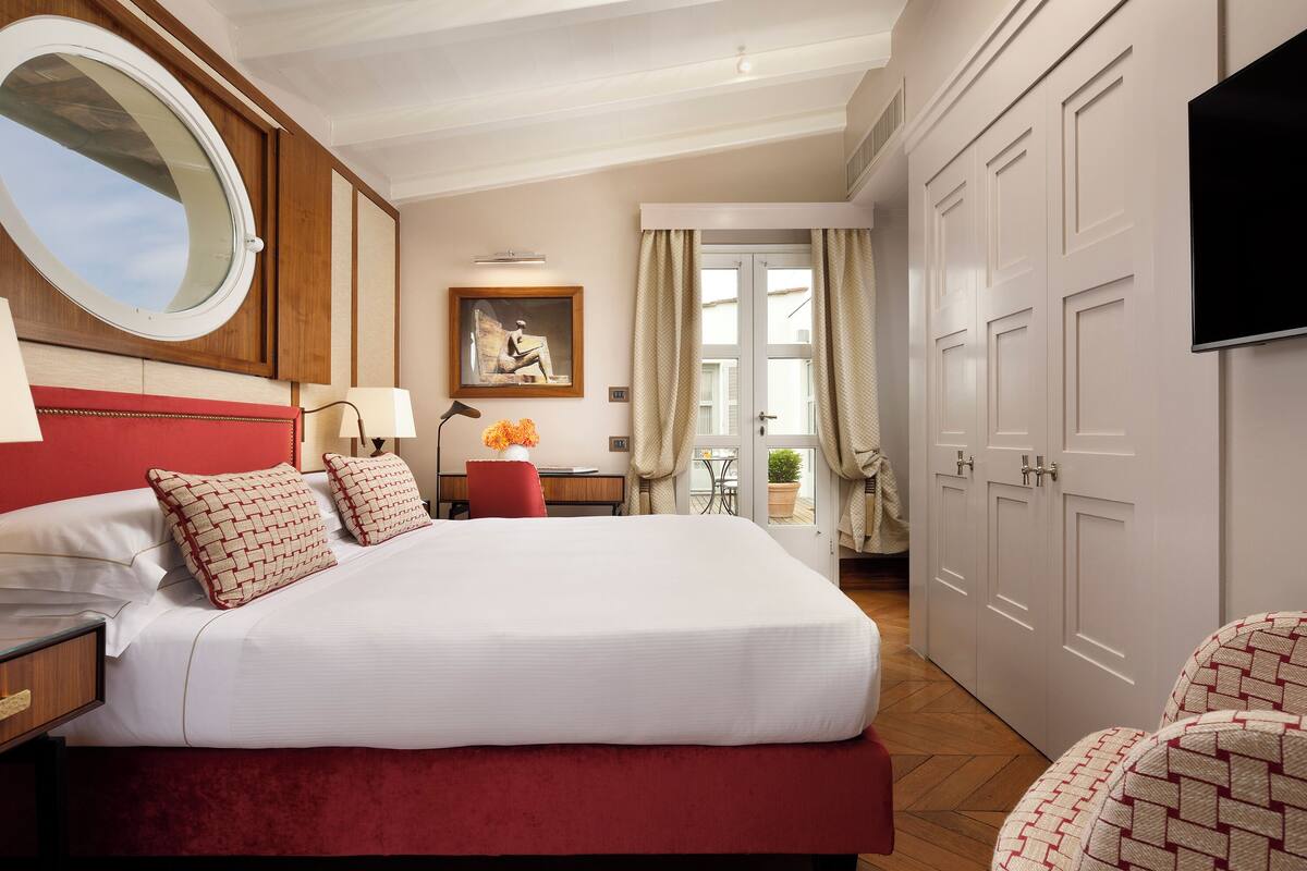 A hotel room with a large bed, a desk with a lamp, a painting, a television, and a wardrobe.