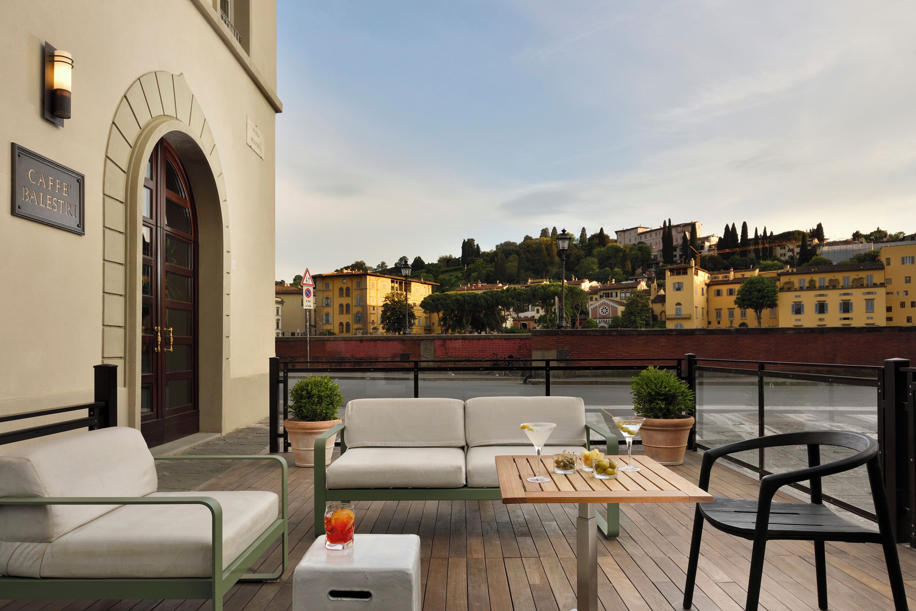 Un área de estar al aire libre con sofá, sillas y una mesa, con vistas a un paisaje urbano que incluye edificios y un río.