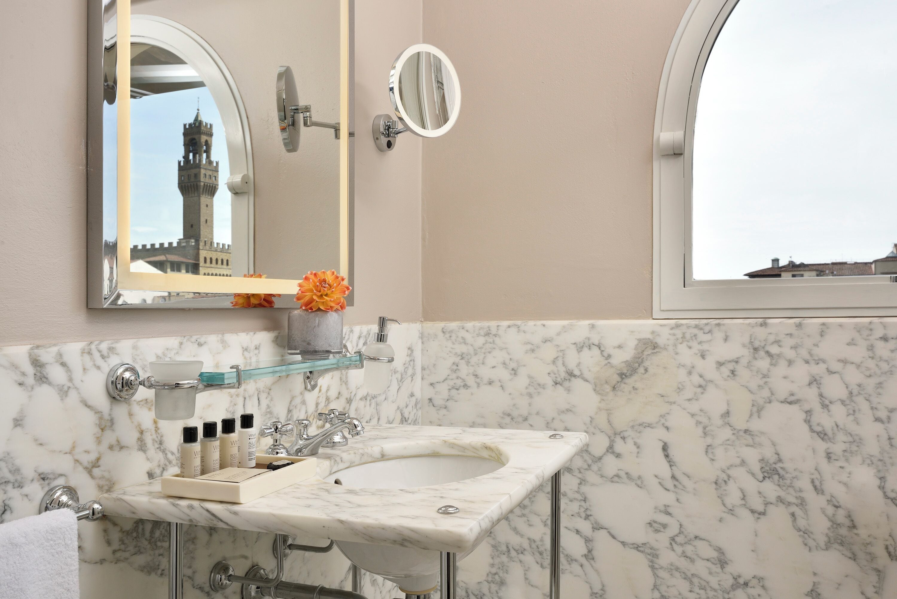 A bathroom with a marble sink, a mirror, and a window with a view of a tower.