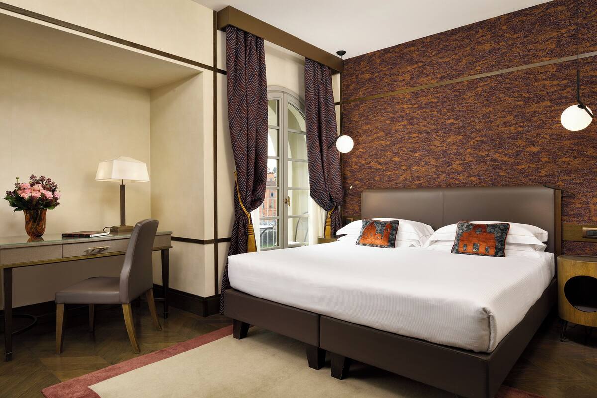 A hotel room with a bed, desk, chair, and a view of the outside.