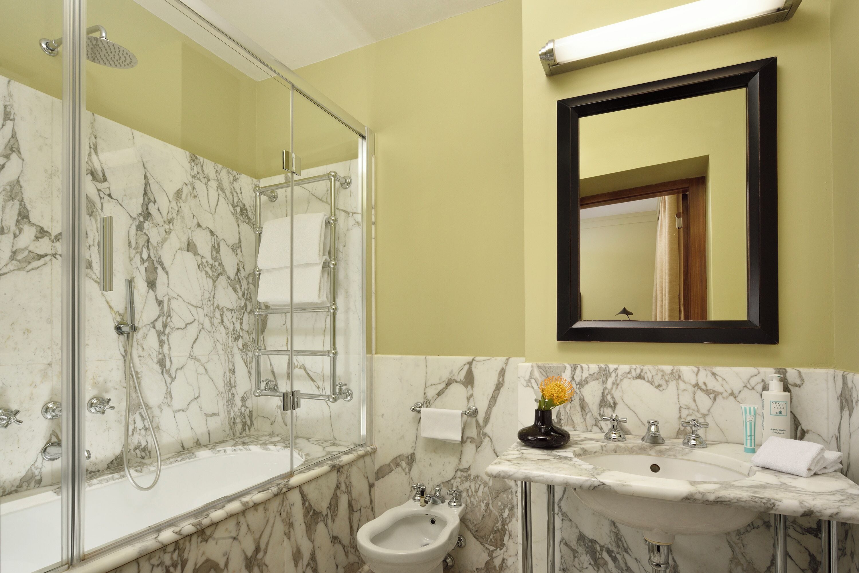 A bathroom with a glass-enclosed shower, a bidet, and a sink with a marble countertop.