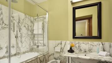 A bathroom with a glass-enclosed shower, a bidet, and a sink with a marble countertop.