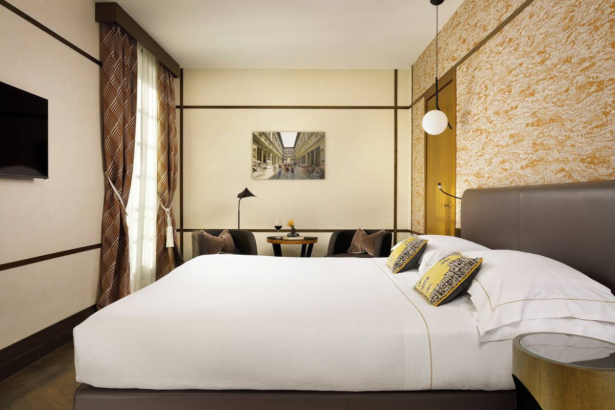 A hotel room with a large bed, a desk with a chair, a flat-screen TV, a lamp, and a painting on the wall.