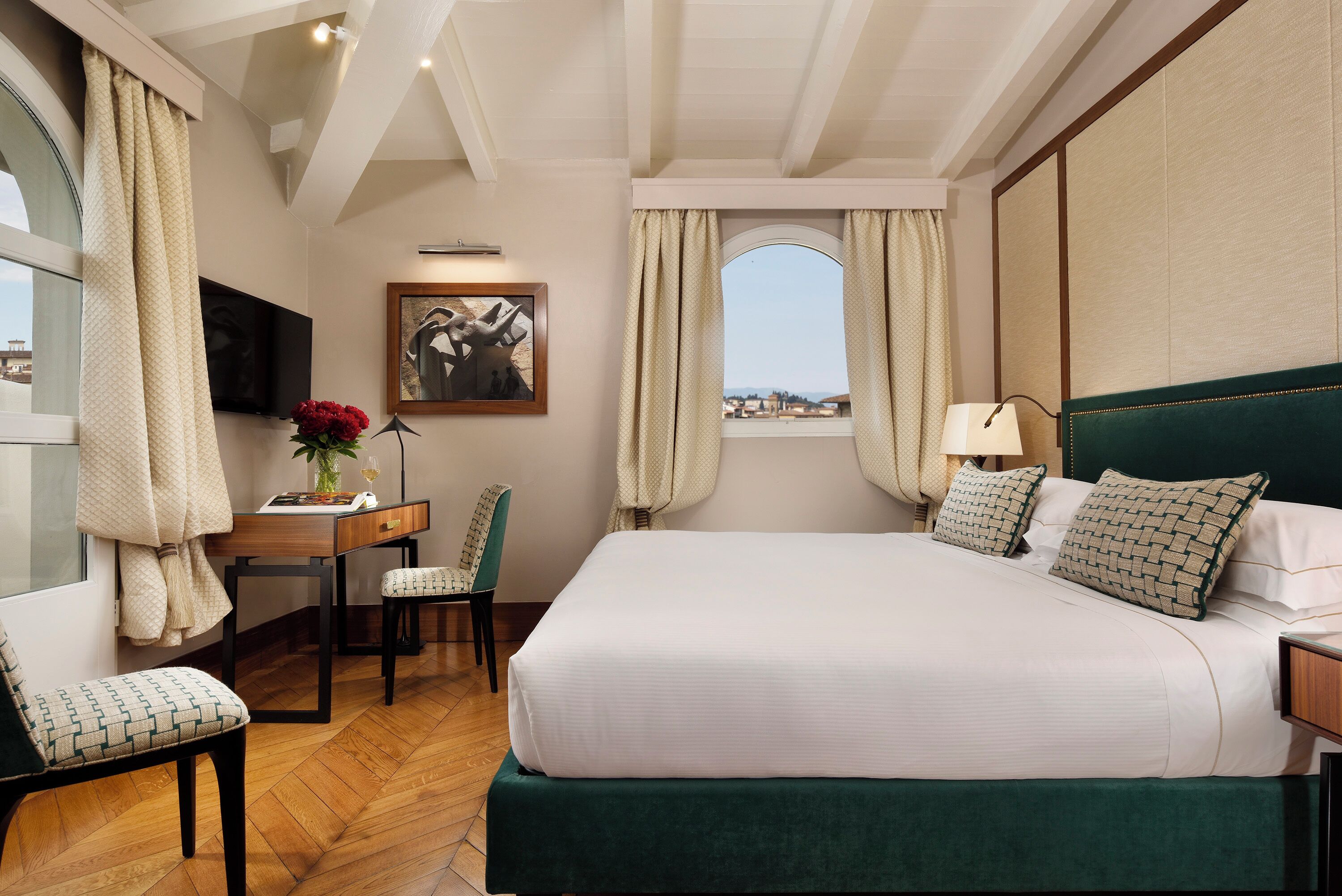 A hotel room with a large bed, a desk with a chair, a TV, and a window with curtains.