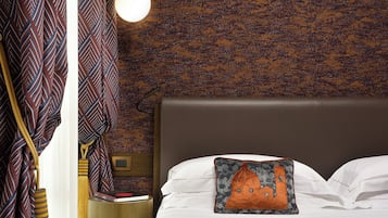 A neatly made bed with a pillow featuring a building design, a bedside lamp, and a wall with a textured pattern.
