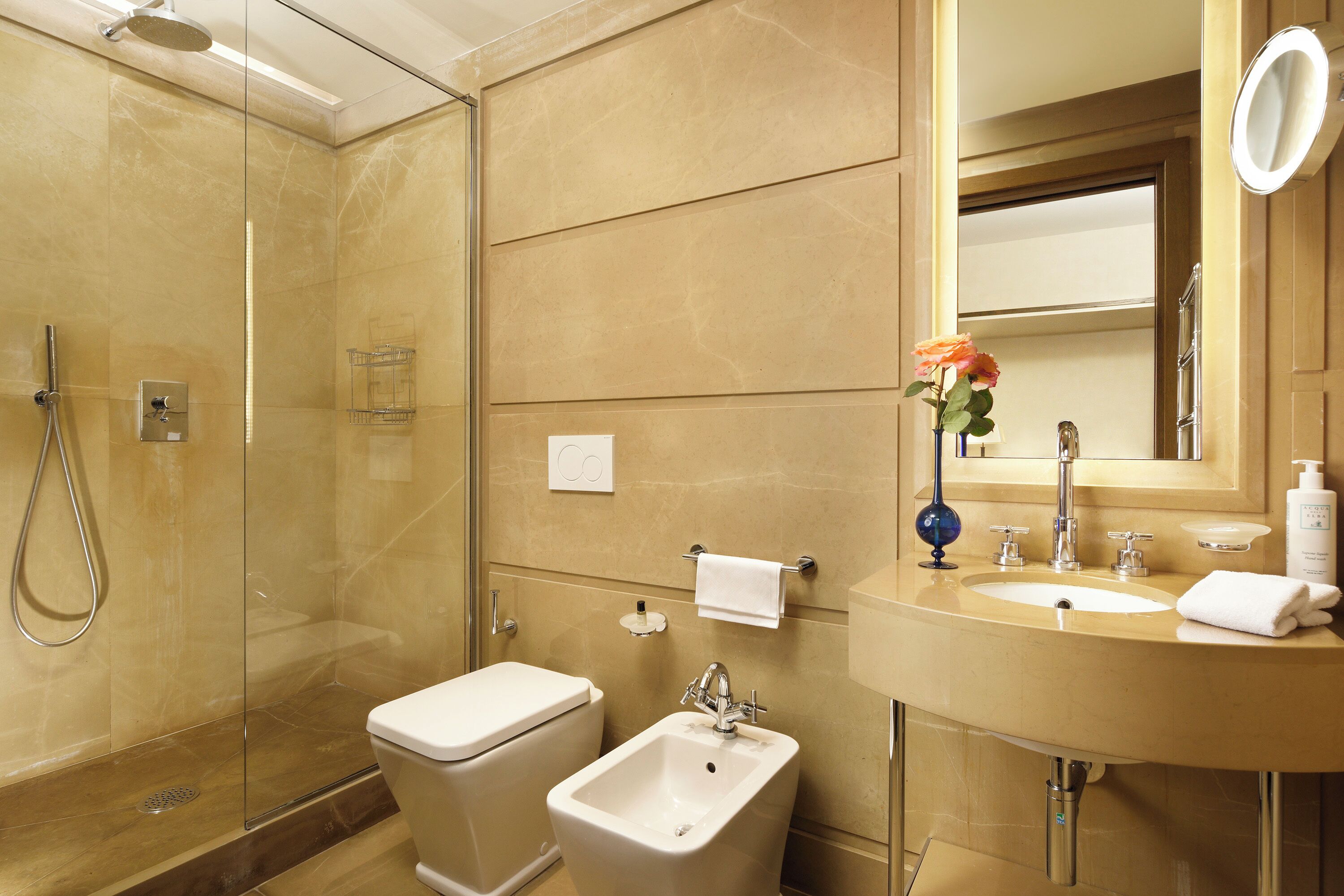Une salle de bain moderne dotée d’une douche à parois de verre, d’un bidet, d’un lavabo avec un miroir et d’un vase rempli de fleurs.