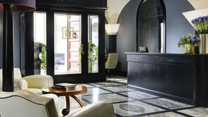 A lobby with a reception desk, seating area, and large windows with views of the outside. - Hotel Balestri (Florence)
