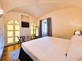 A hotel room with a large bed, a television mounted on a cabinet, a desk with a chair, and a window with curtains.