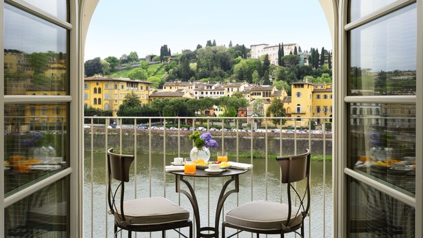 A balcony with two chairs and a table, overlooking a river with buildings in the background. - Hotel Balestri (Florence)