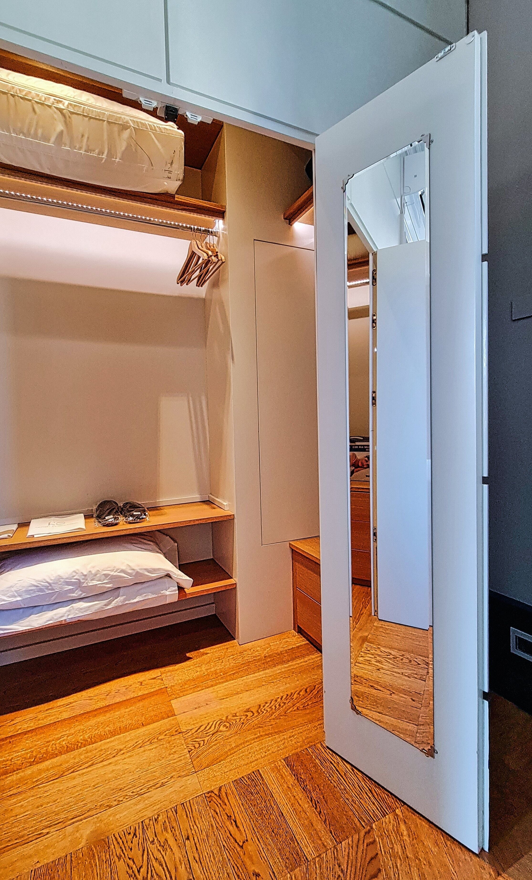 A compact room with a bunk bed, a small wooden shelf, and a door leading to another room.