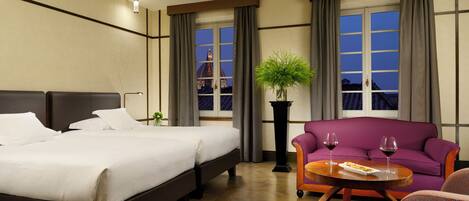 Ein Hotelzimmer mit einem großen Bett, einem Schlafsofa, einem kleinen Tisch mit Weingläsern und einer Topfpflanze.