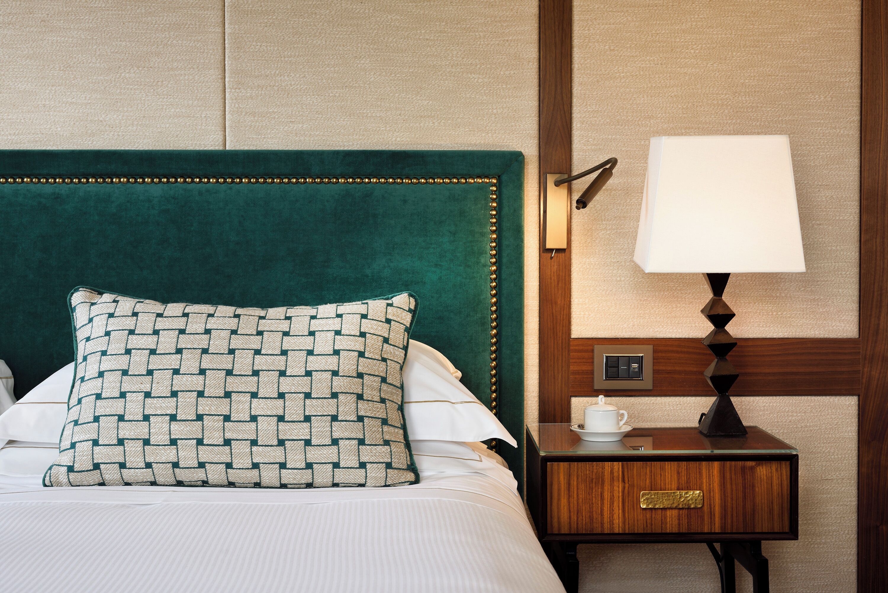 A neatly made bed with a patterned pillow, a bedside table with a lamp, and a cup.