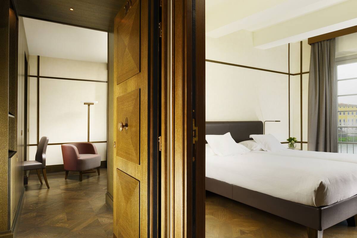 A hotel room with a large bed, a chair, and a wooden wardrobe.