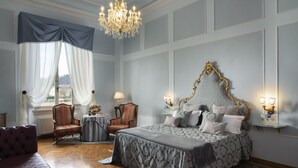 Een slaapkamer met een groot bed, een kroonluchter, een raam met gordijnen, een stoel en een nachtkastje.