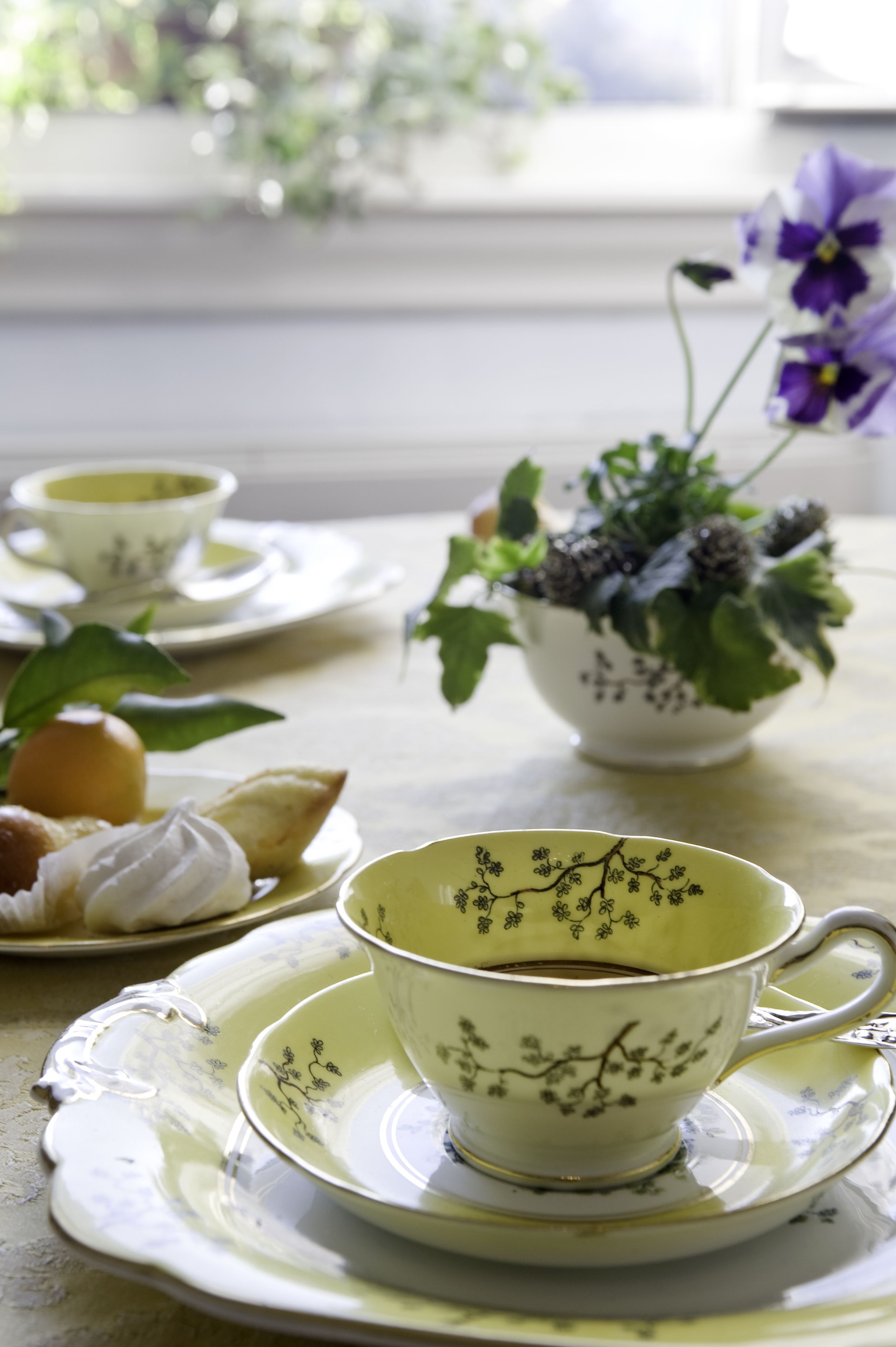 Una mesa con un juego de té, un cuenco de flores y una bandeja con pasteles.