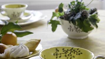 Una mesa con un juego de té, un cuenco de flores y una bandeja con pasteles.