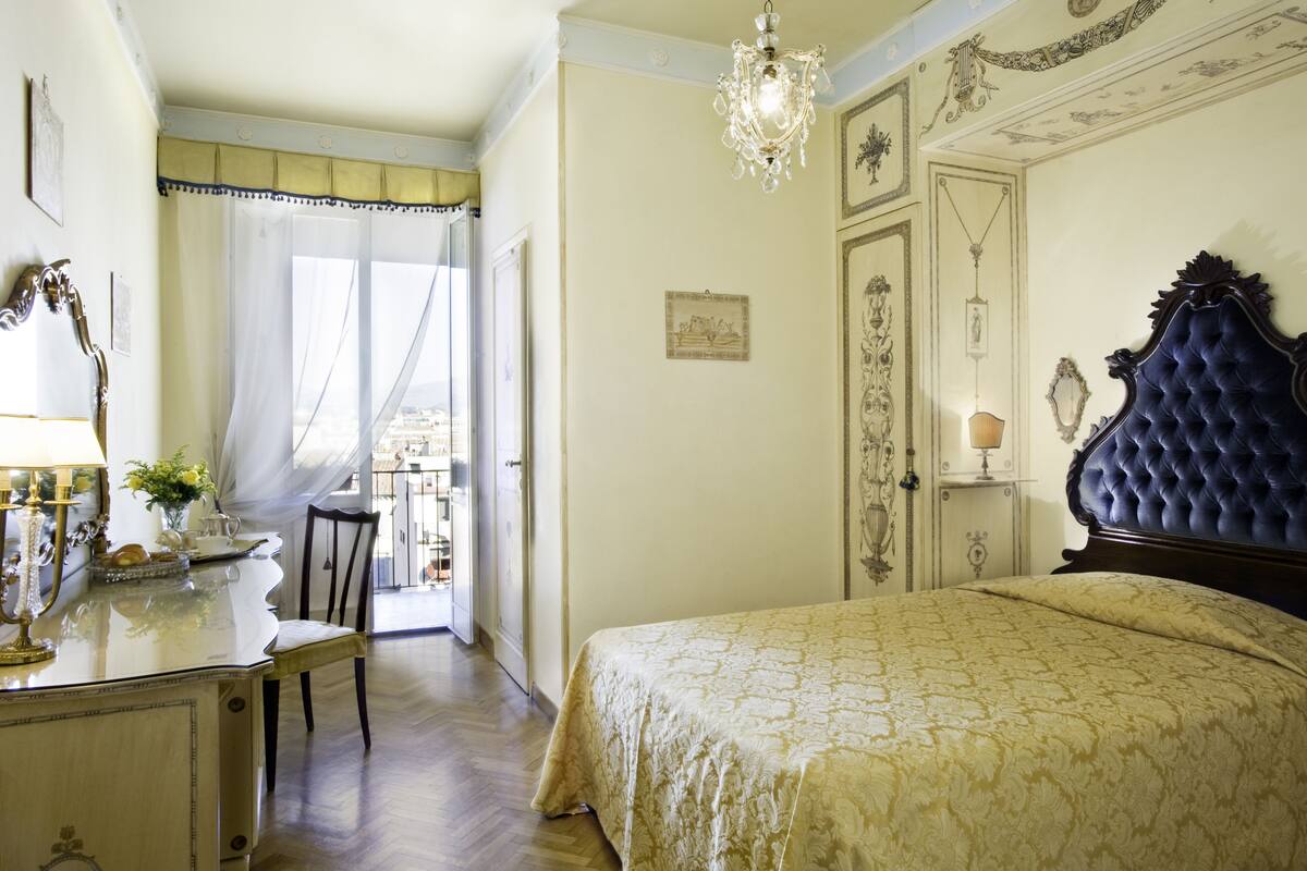A bedroom with a large bed, a chandelier, and a desk with a lamp.