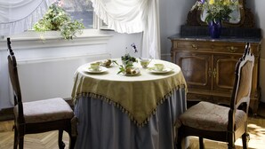 Een kamer met een ronde tafel gedekt voor thee, twee stoelen, een spiegel en een raam met gordijnen.