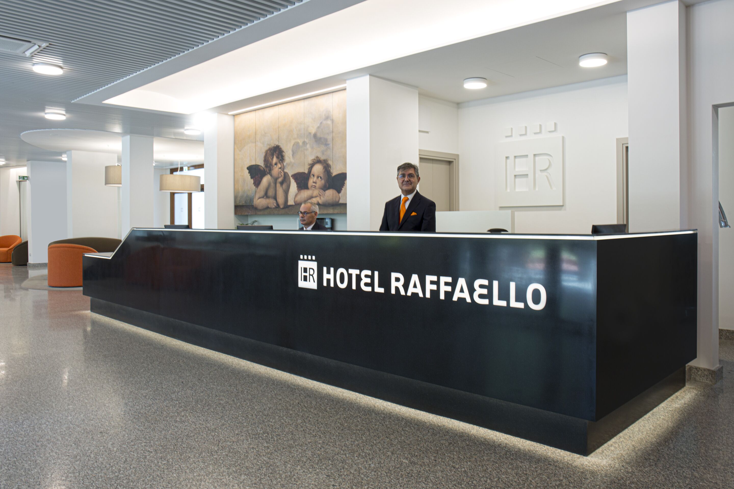 Un comptoir d’accueil à l’hôtel RAFFAELLO, doté d’un design moderne, d’un logo et d’un grand tableau accroché au mur.