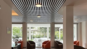 A modern lobby with a polished floor, a ceiling with linear patterns, and a seating area with chairs and a table. - Hotel Raffaello (Florence)