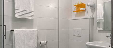 A modern bathroom with a toilet, sink, and shower. There are towels and a hairdryer on the wall.