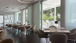 A modern restaurant with high ceilings, circular ceiling lights, and large windows offering views of the outdoors. - Hotel Raffaello (Florence)