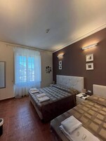 Una habitación de hotel con cama, sofá, mesita de noche, lámpara y ventana con cortinas.