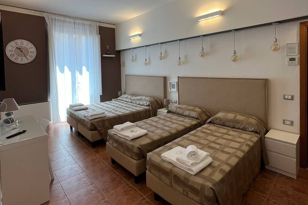 Une chambre d’hôtel avec deux lits, un bureau, une horloge et une fenêtre avec des rideaux.
