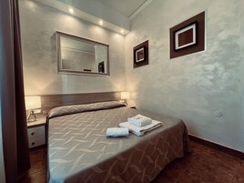 Quarto de hotel com uma cama, uma mesa de cabeceira, um abajur, um espelho e dois quadros na parede.