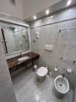 A modern bathroom with a marble sink, a toilet, a bidet, and a hand dryer mounted on the wall.
