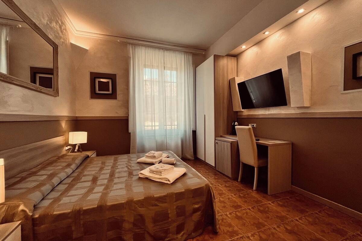 Une chambre d’hôtel avec un lit, un bureau, une chaise, une télévision et une fenêtre avec des rideaux.