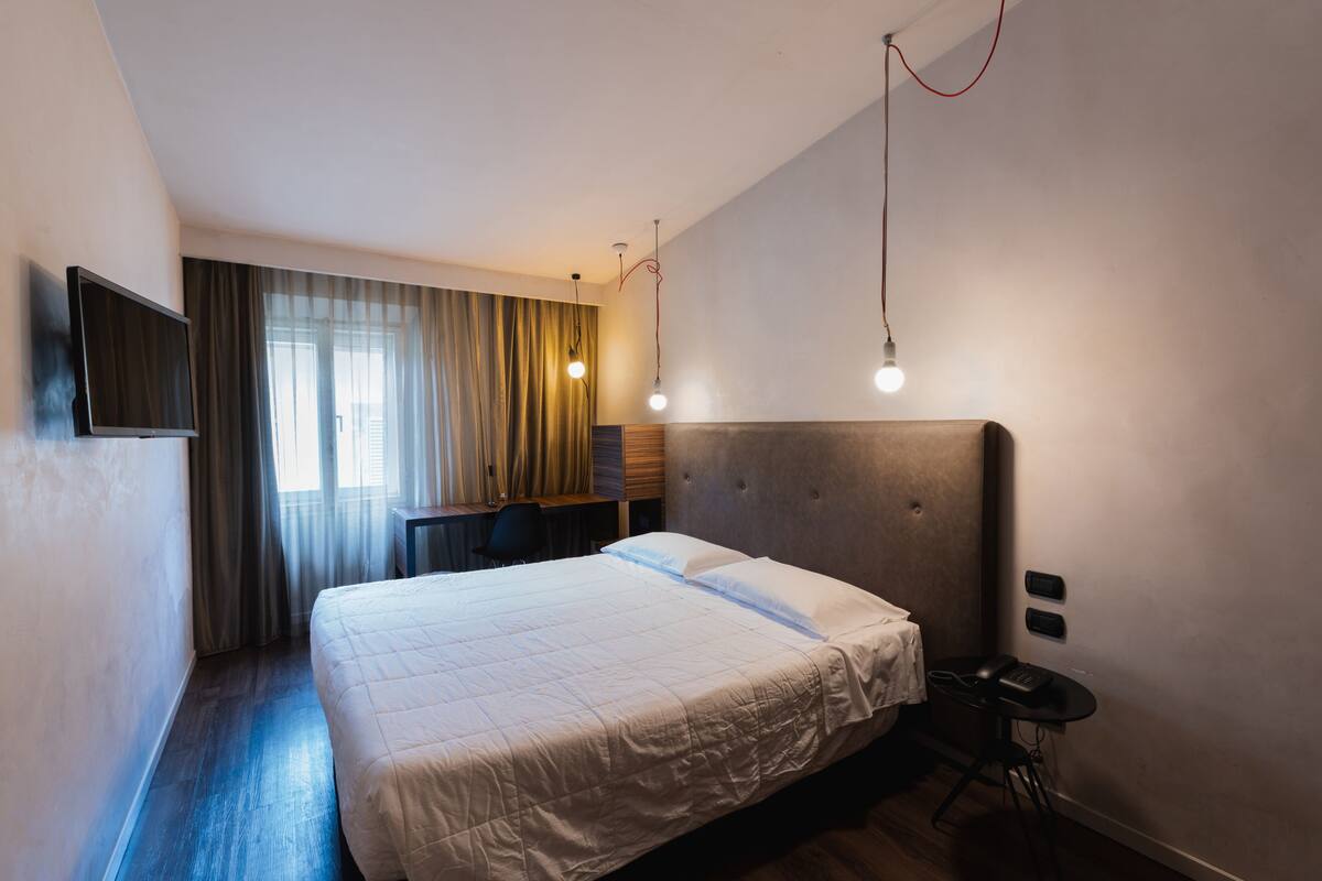 A modern hotel room with a large bed, a desk, and a chair.