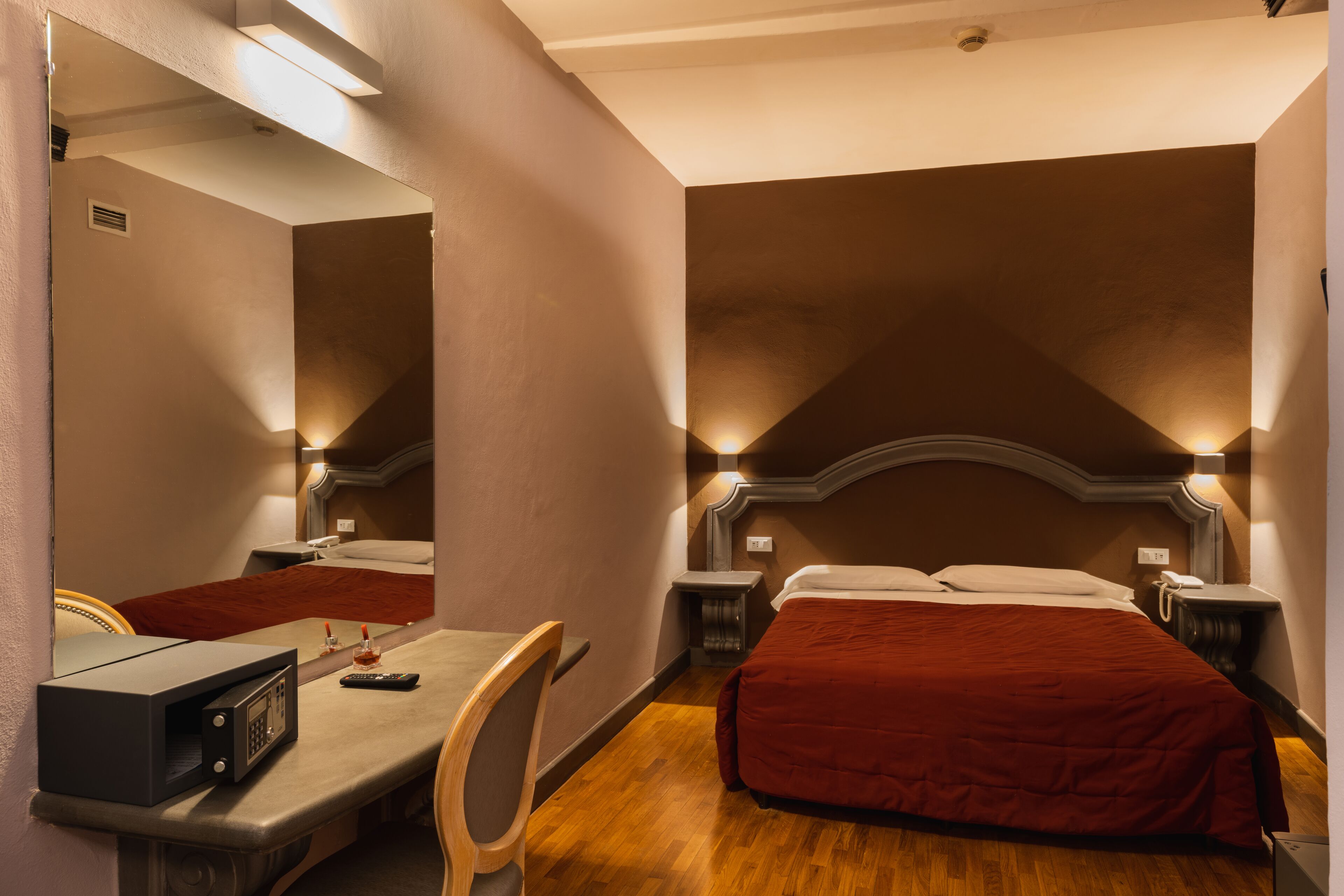 A hotel room with a bed, bedside tables, a desk with a chair, a microwave, and a mirror.