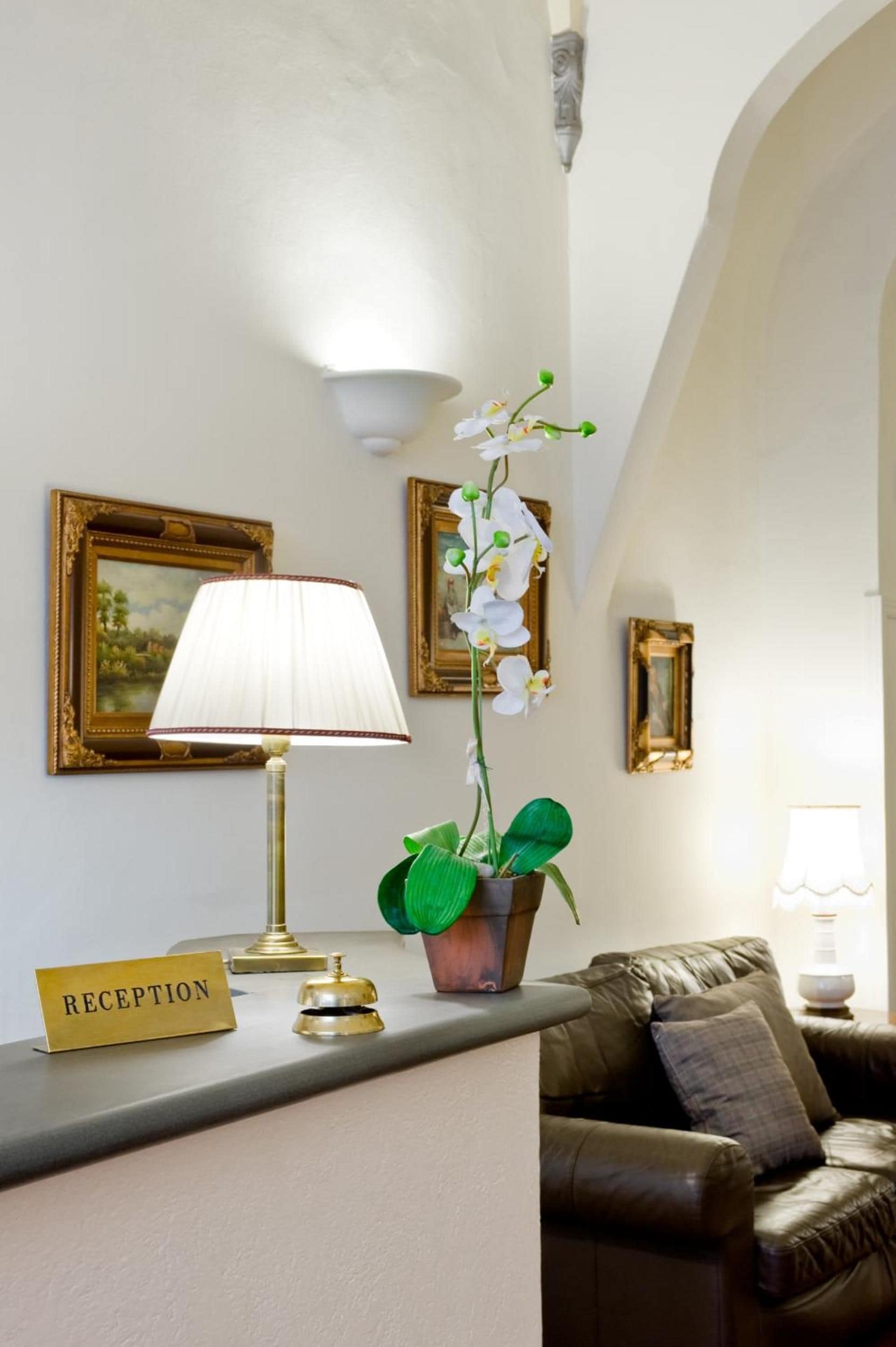 Un área de recepción con mostrador, una lámpara, una orquídea en maceta y obras de arte enmarcadas en la pared.