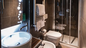 A modern bathroom with a large sink, two toilets, a glass shower enclosure, and a vanity with a mirror and lights. - Hotel Unicorno (Florence)