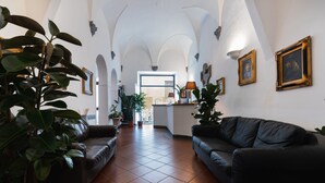 A spacious living room with a black leather sofa, a coffee table, and potted plants. There are tiled floors and a large window providing natural light. - Hotel Unicorno (Florence)
