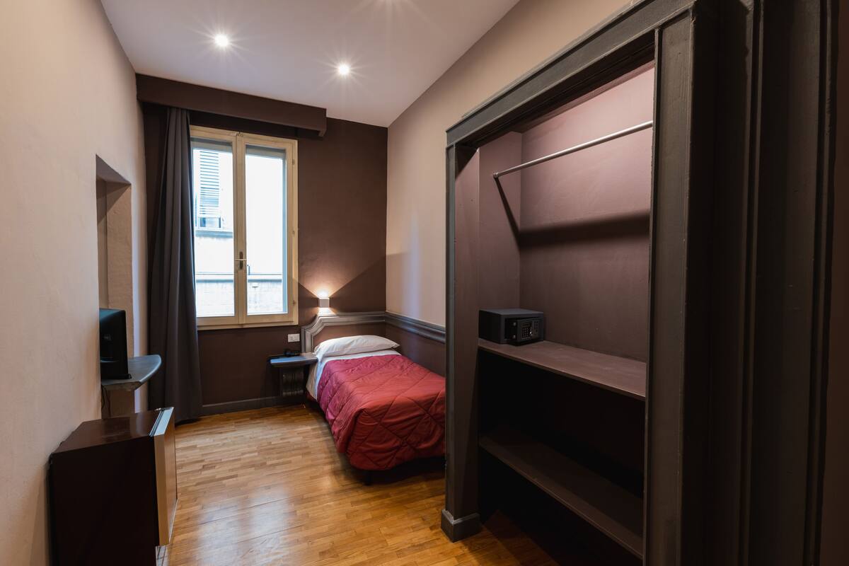 A compact bedroom with a bed, bedside table, lamp, and a wardrobe.
