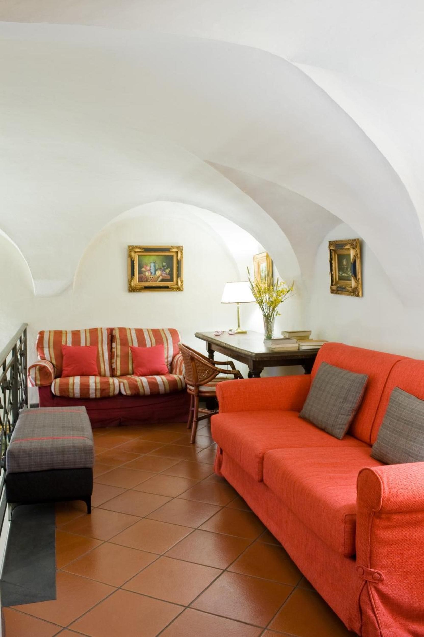 Ein Wohnzimmer mit einem roten Sofa, einem gestreiften Sofa und einem kleinen Tisch mit Lampe und Vase.