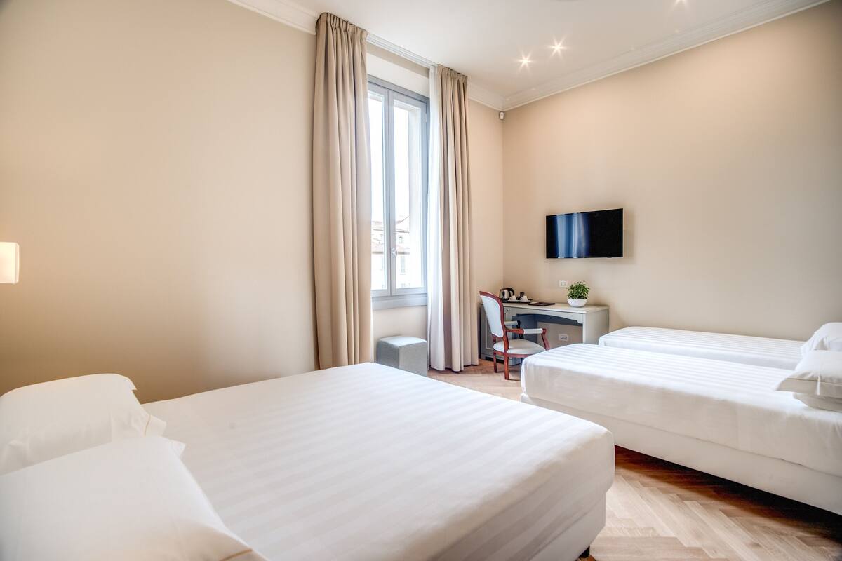 Habitación de hotel con dos camas, un escritorio, una silla, un televisor y una ventana con cortinas.