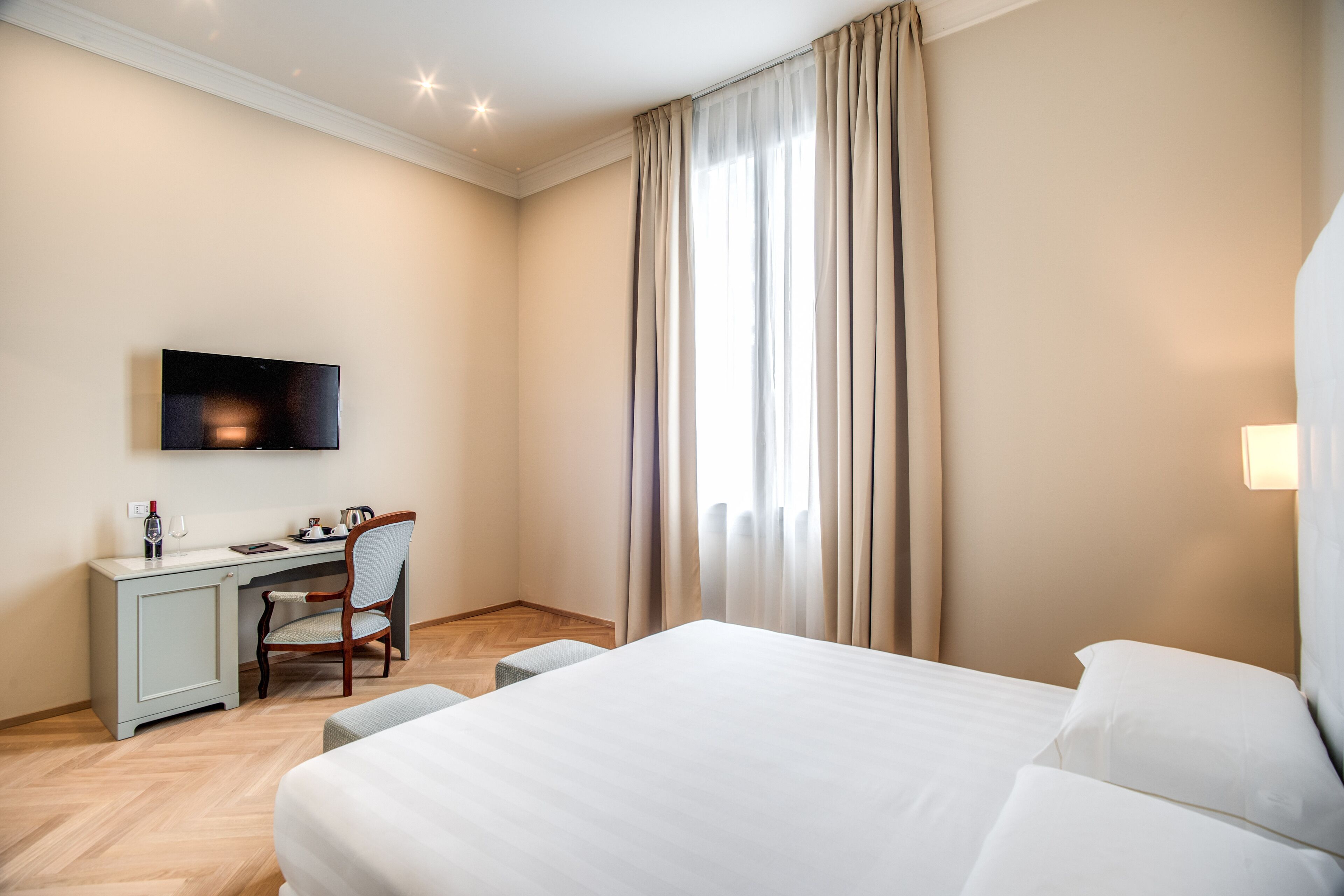 A hotel room with a bed, a desk, a chair, a television, and a window with curtains.